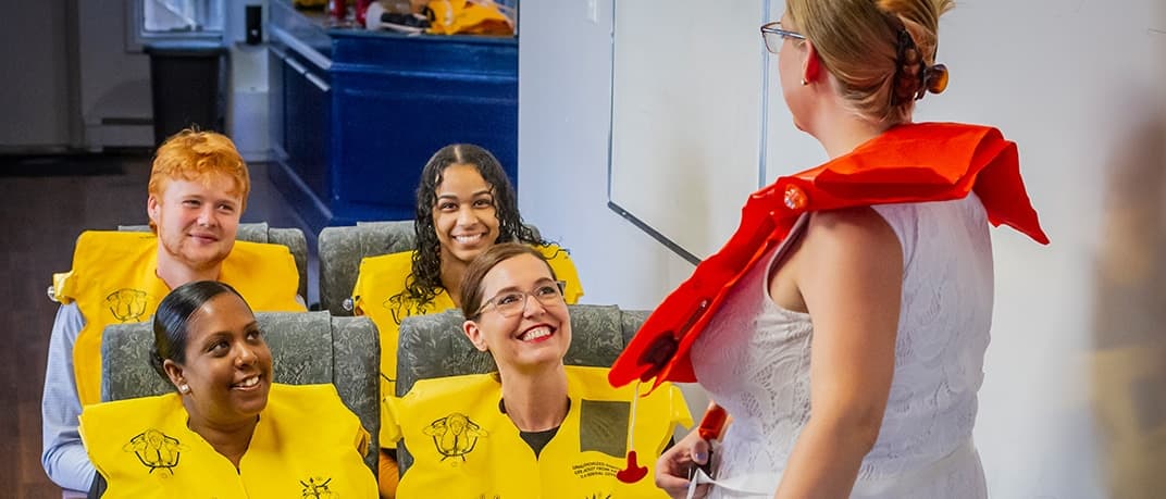 Estudiantes con chalecos salvavidas practicando procedimientos de seguridad con una instructora, programa de Atlantic Flight Attendant Academy