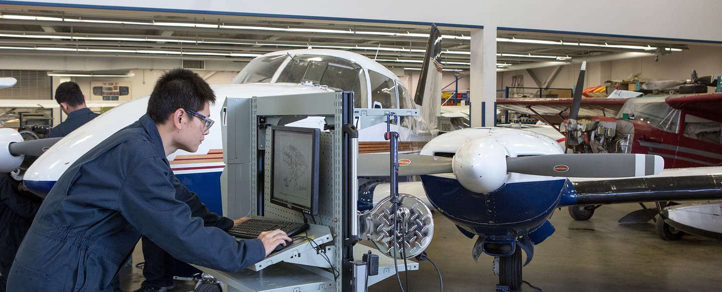 Estudiante de Centennial College trabajando en un sistema de diagnóstico de aviónica junto a una aeronave