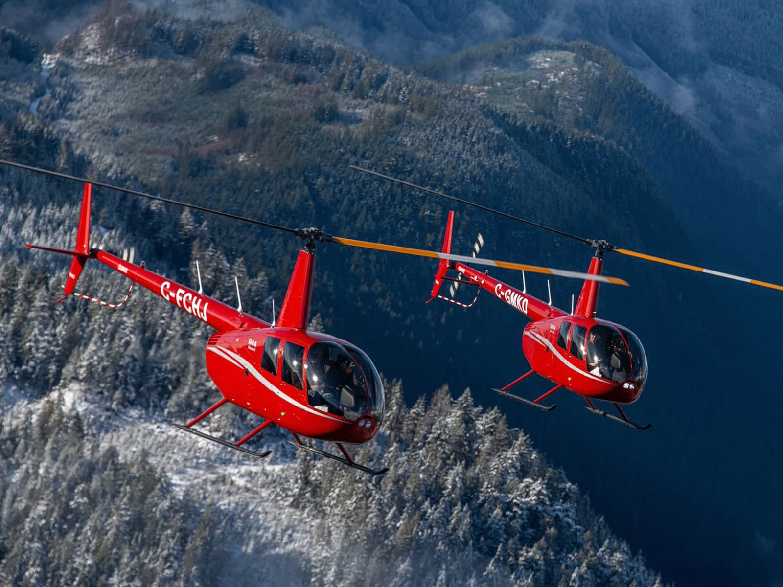 Dos helicópteros Robinson R44 de Chinook Helicopters volando sobre montañas nevadas de BC