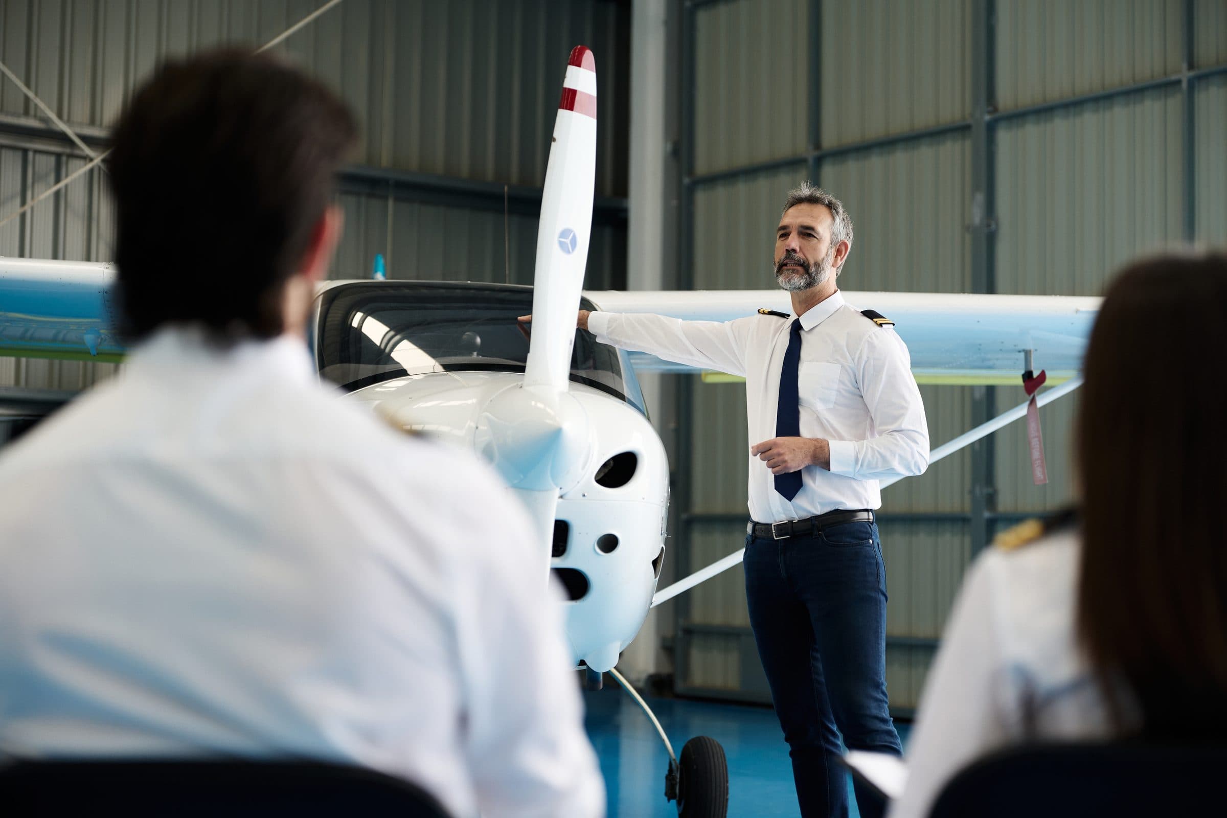 Instructor de vuelo explicando la hélice de una avioneta a sus estudiantes en un hangar