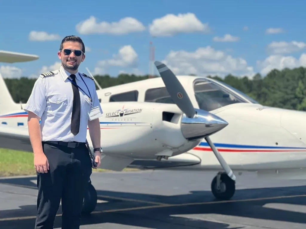 Piloto en uniforme frente a una aeronave multimotor Piper Seminole con el logo de Select Aviation
